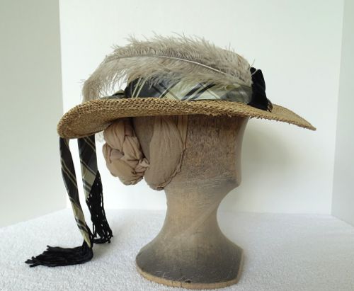 The hat band is made of plaid silk taffeta in neutral shades and there is a long natural ostrich feather that goes from the front to the back on the right side.